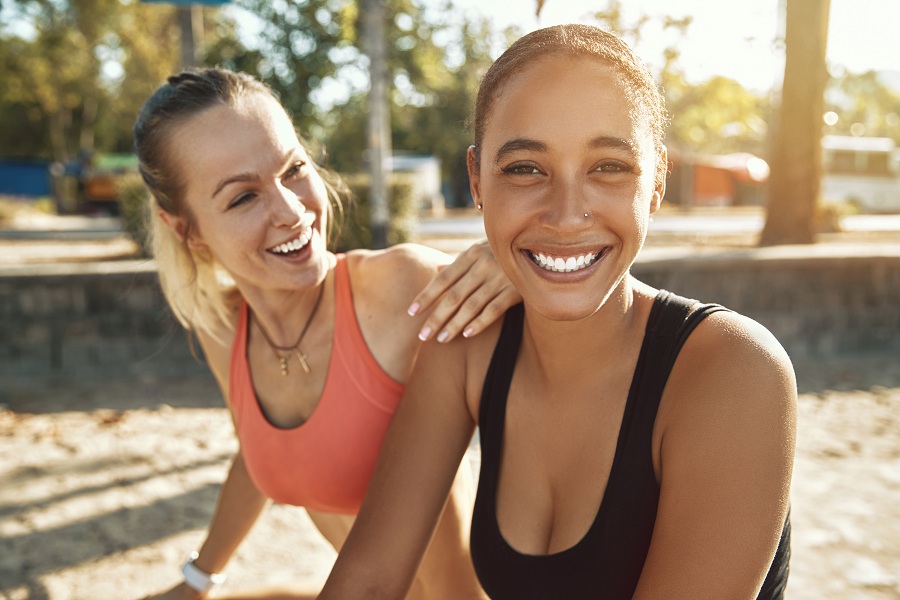 Two women laughing while taking a break from exercising outside