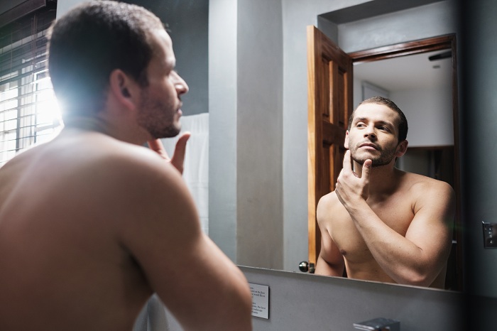 Shirtless Man Looks at Himself in Front of Mirror